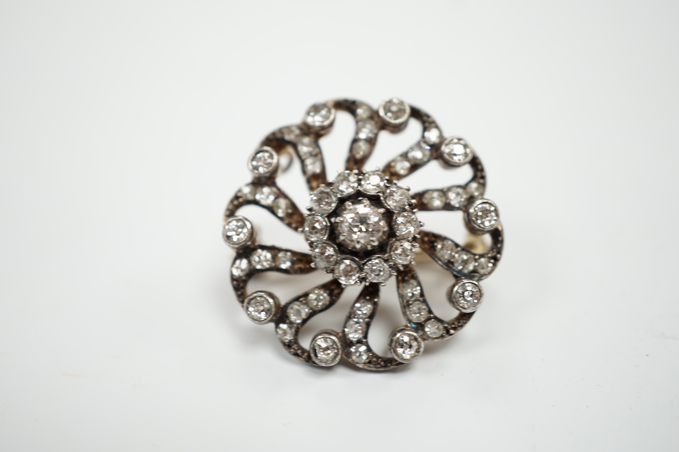 A Victorian yellow metal and diamond cluster set whorl shaped brooch, scrolling border and detachable brooch attachment, 25mm, gross weight 8.7 grams.